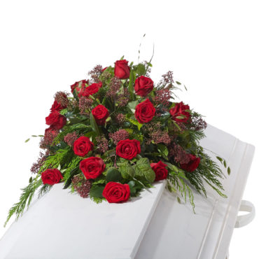 Begravningsblommor bestående av röda rosor samt grönt utfyllnad liggandes på vit kista.