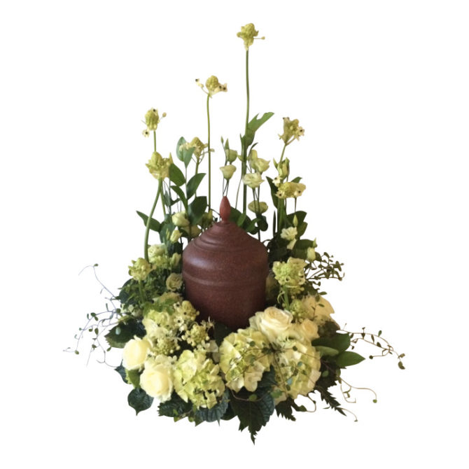 Liten brun urn som har vita och lime färgade begravningsblommor, samt grönt omkring sig. Urnen är i mitten av urndekorationen och blommorna omfamnar vackert urnen.