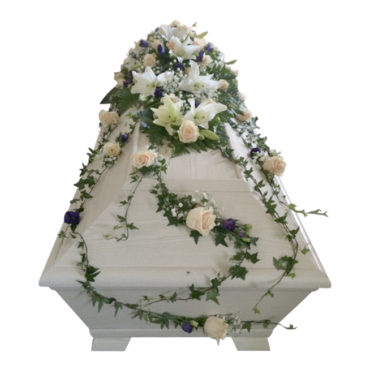 Begravningsblommor på vit begravningskista,blommorna består av champagnerosor, vita liljor, lila prärieklocka, brudslöja samt murgröna som hänger ner över kistan som en kistdekoration.