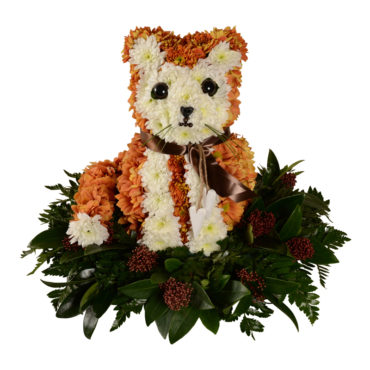 Personligt arrangemang begravningsblomma gjord av orangea och vita blommor som formar en katt. Katten sitter på flera blad. och har även ett brunt silkesband runt halsen.